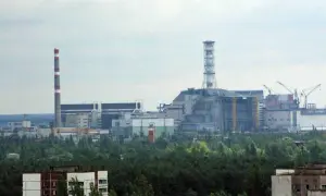 Widok na elektrownię w Czarnobylu, z charakterystycznym kominem i budynkami przemysłowymi otoczonymi lasem.