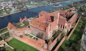 Malbork, największy zamek na świecie, rozciąga się wzdłuż rzeki Nogat. Potężne ceglane mury i wieże świadczą o jego historycznym znaczeniu.