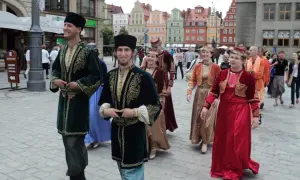Ludzie w tradycyjnych strojach, przypominających ubiory karaimów w Polsce, spacerują po brukowanym placu.