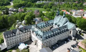 Widok z lotu ptaka na klasztor na Górze Świętej Anny. Rozległy kompleks budynków z zielonymi dachami otoczony bujną zielenią.
