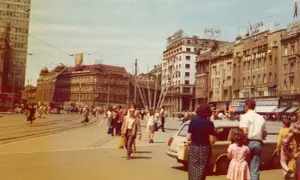 Tłoczny plac w Jugosławii, ludzie spacerują, jeżdżą tramwaje i samochody.