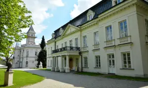 Pałac Radziejowice noclegi cennik: biały pałac z wieżą, zielony trawnik, rzeźby, drzewa, błękitne niebo z chmurami.