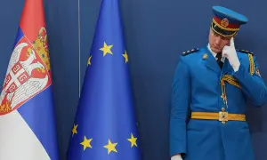 Strażnik w niebieskim mundurze zastanawia się, czy Serbia jest w Unii, stojąc obok flag Serbii i UE.
