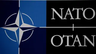 Symbol NATO i napis "NATO OTAN" na czarnym i niebieskim tle. Powstanie NATO to ważny moment w historii.