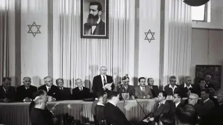 Uroczystość ogłoszenia powstania państwa Izrael. Na ścianie portret Herzla i gwiazdy Dawida.