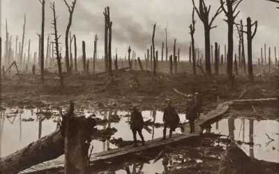 Żołnierze idą po drewnianych kładkach przez błotniste, zniszczone tereny po bitwie pod Ypres. W tle widać zgliszcza i martwe drzewa.