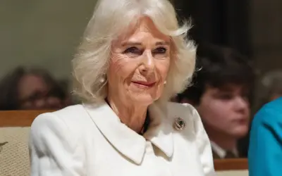 Uśmiechnięta królowa Camilla w białym płaszczu z broszką.