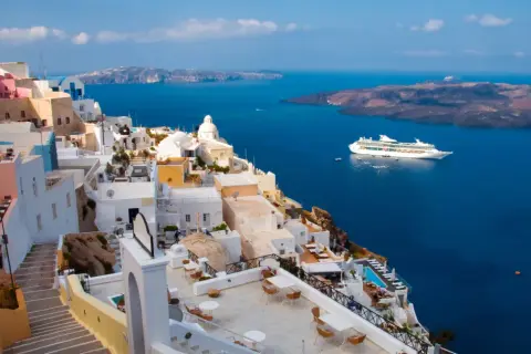 Santorini, Grecja. Białe domy na klifie, błękitne morze i statek wycieczkowy. Planujesz podróż? Pamiętaj o podatku turystycznym Grecja.