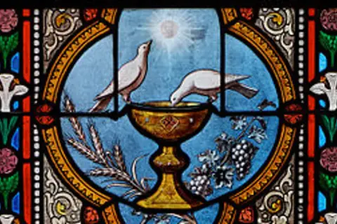 Witraż przedstawia kielich, z którego piją gołębice, symbolizujący święty graal. Obok kłosy i winogrona.