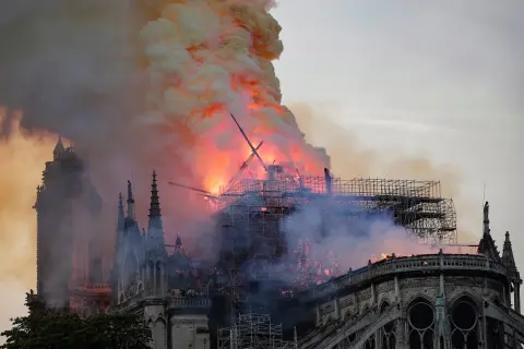 Notre Dame pożar: płomienie trawią dach katedry, unoszą się kłęby dymu. Widoczne rusztowania i zniszczona konstrukcja.