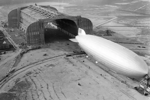 Ogromny hangar lotniczy i sterowiec Hindenburg na płycie lotniska.