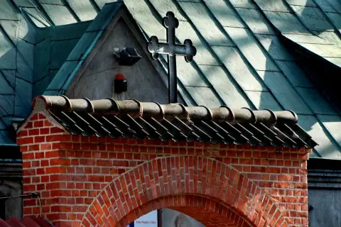Ceglany łuk i dach kościoła z krzyżem. Nawet apostata mógłby tu znaleźć spokój, patrząc na te dachówki.