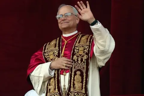 Papież w bogato zdobionej szacie pozdrawia wiernych. Jego uśmiech i gest ręki budzą nadzieję, a jego strój przypomina o tym, skąd pochodzi papież i jego dziedzictwo.