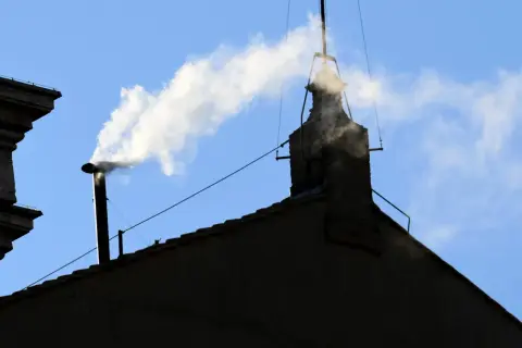 Biały dym z komina, jak sygnał wyboru nowego papieża, unosi się na tle błękitnego nieba.