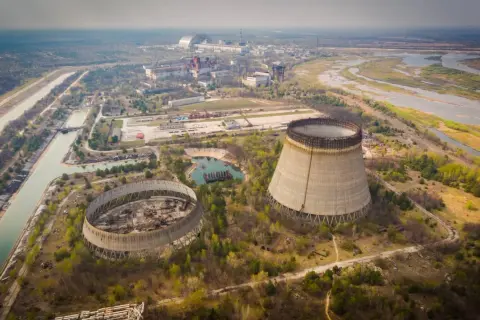 Widok na opuszczoną elektrownię atomową, gdzie doszło do katastrofy w Czarnobylu. Widać niedokończone wieże chłodnicze i rozległy teren.