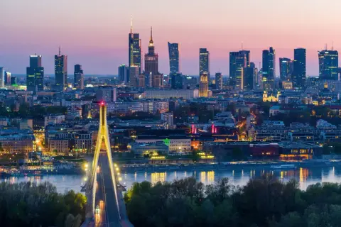 Warszawa nocą, z mostem i wieżowcami. Miasto tętni życiem, a jego warszawa liczba mieszkańców stale rośnie.