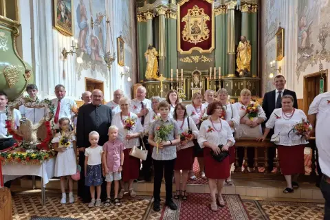 Uroczystość Wniebowzięcia Najświętszej Maryi Panny w kościele. Grupa osób w strojach ludowych i duchowny pozują do zdjęcia.