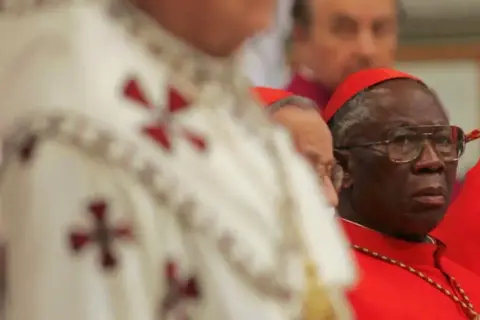 Kardynał w okularach, w czerwonej sutannie, obok duchownego w białej szacie z krzyżami. Może to być przyszły czarny papież.