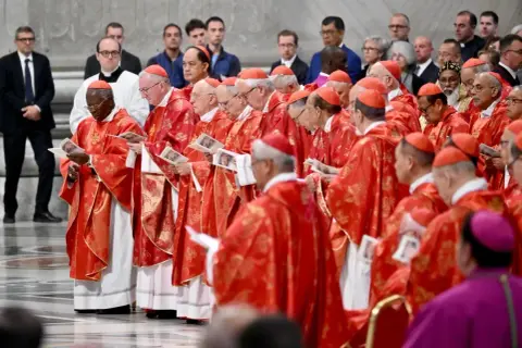 Kardynałowie w czerwonych szatach, przygotowujący się do wyboru papieża, trzymają w rękach dokumenty.
