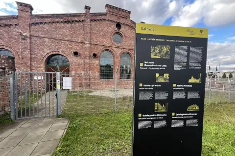 Tablica informacyjna Szlaku Zabytków Techniki w Katowicach, obok ceglanej budowli dawnej huty.
