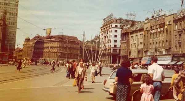 Tłoczny plac w Jugosławii, ludzie spacerują, jeżdżą tramwaje i samochody.