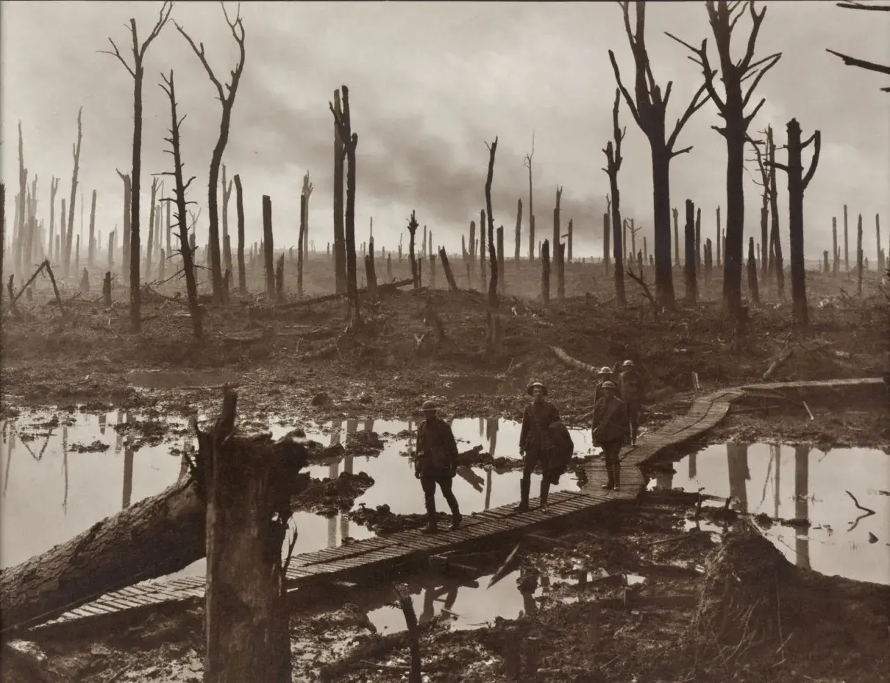 Żołnierze idą po drewnianych kładkach przez błotniste, zniszczone tereny po bitwie pod Ypres. W tle widać zgliszcza i martwe drzewa.