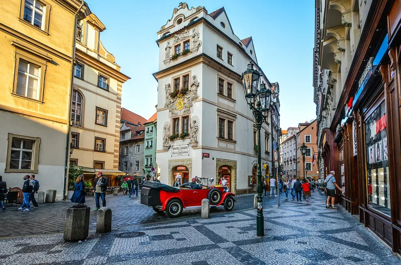 Uliczka w Pradze z zabytkowym czerwonym kabrioletem i budynkiem z napisem "Hotel Aurus Dům Zlaté Střevy".