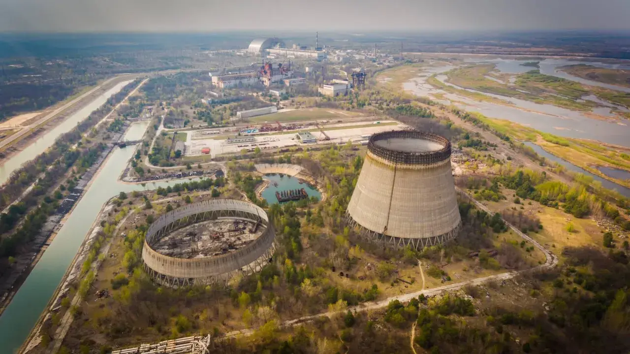 Widok na opuszczoną elektrownię atomową, gdzie doszło do katastrofy w Czarnobylu. Widać niedokończone wieże chłodnicze i rozległy teren.