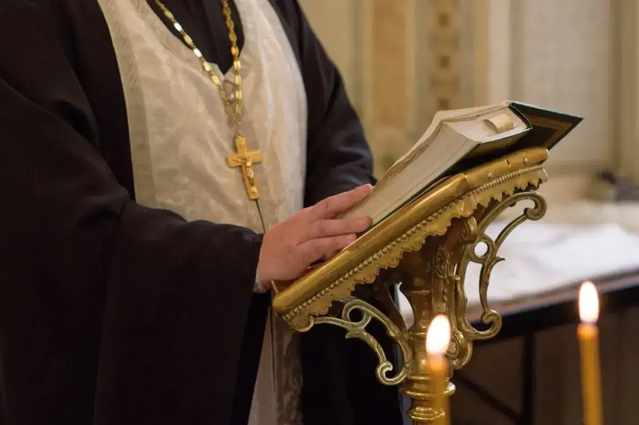 Duchowny w szatach, z krzyżem na szyi, czyta księgę podczas nabożeństwa prawosławnego.