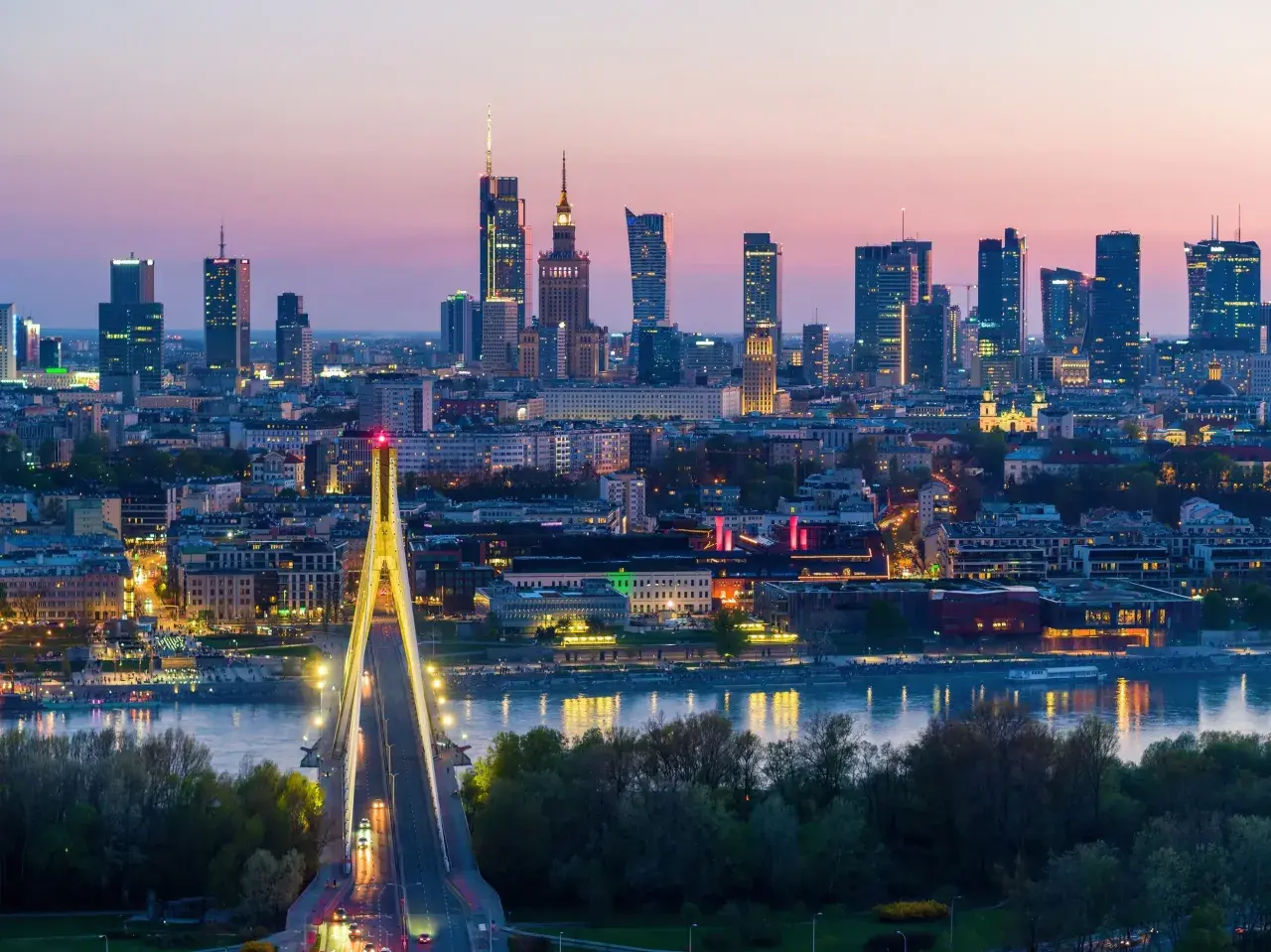 Warszawa nocą, z mostem i wieżowcami. Miasto tętni życiem, a jego warszawa liczba mieszkańców stale rośnie.