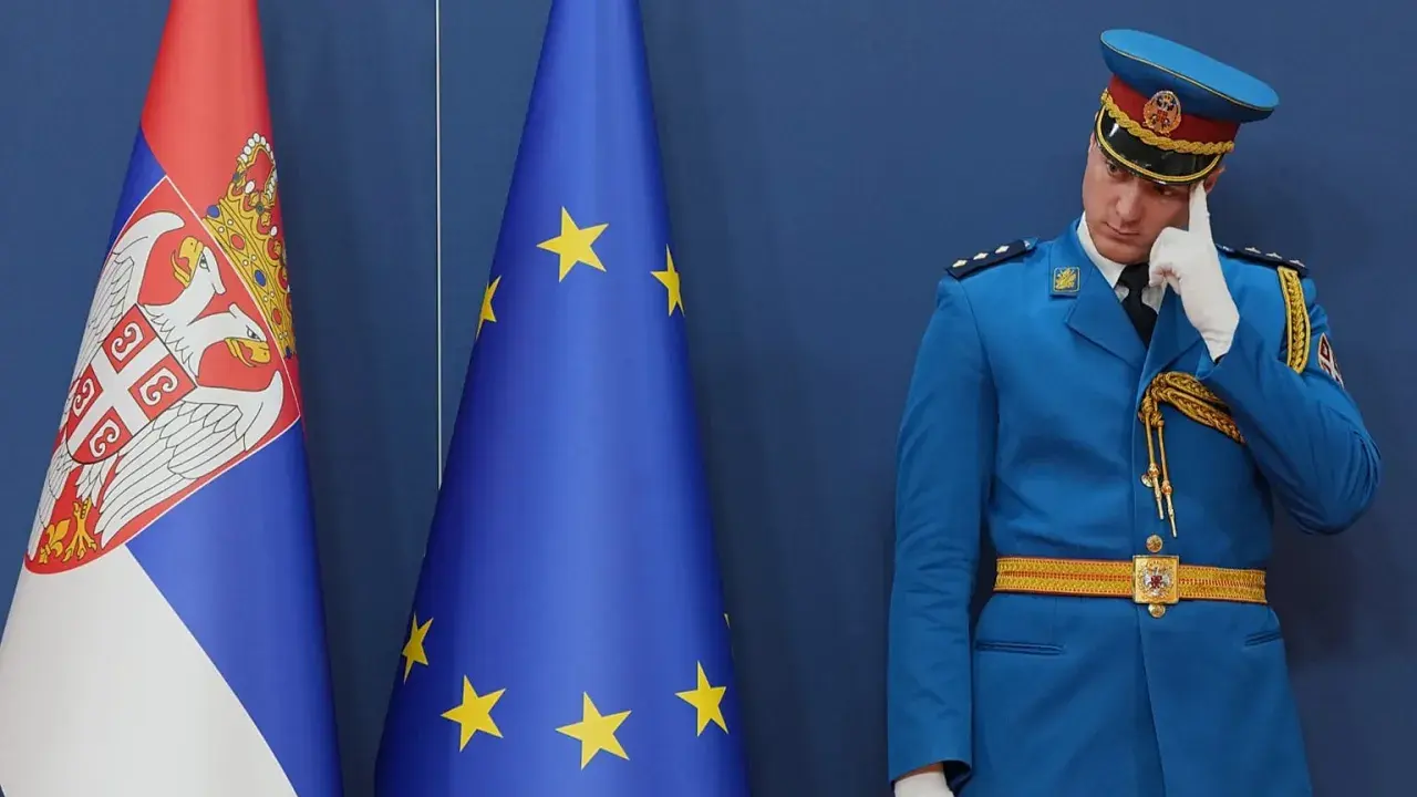 Strażnik w niebieskim mundurze zastanawia się, czy Serbia jest w Unii, stojąc obok flag Serbii i UE.