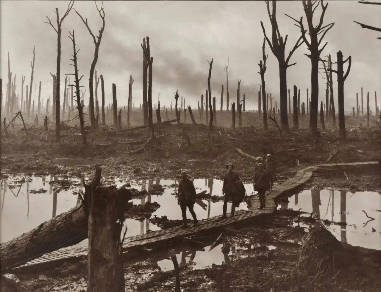 Żołnierze idą po drewnianych kładkach przez błotniste, zniszczone tereny po bitwie pod Ypres. W tle widać zgliszcza i martwe drzewa.