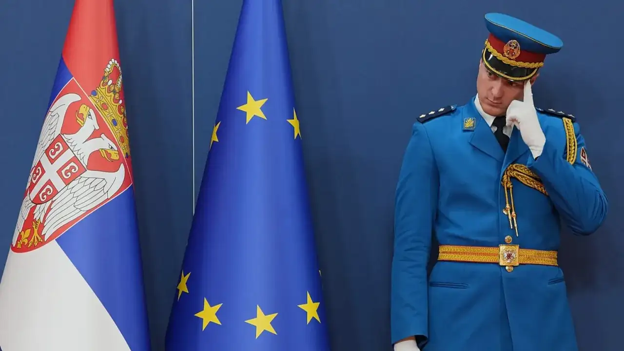 Strażnik w niebieskim mundurze zastanawia się, czy Serbia jest w Unii, stojąc obok flag Serbii i UE.