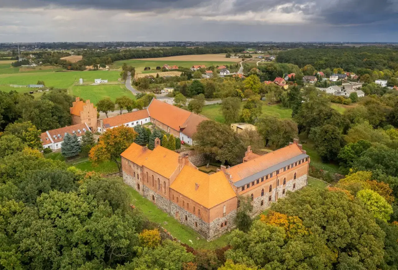 Zamek Bierzgłowski otoczony jesienną zielenią i polami, z charakterystycznymi ceglanymi murami i pomarańczowymi dachami.