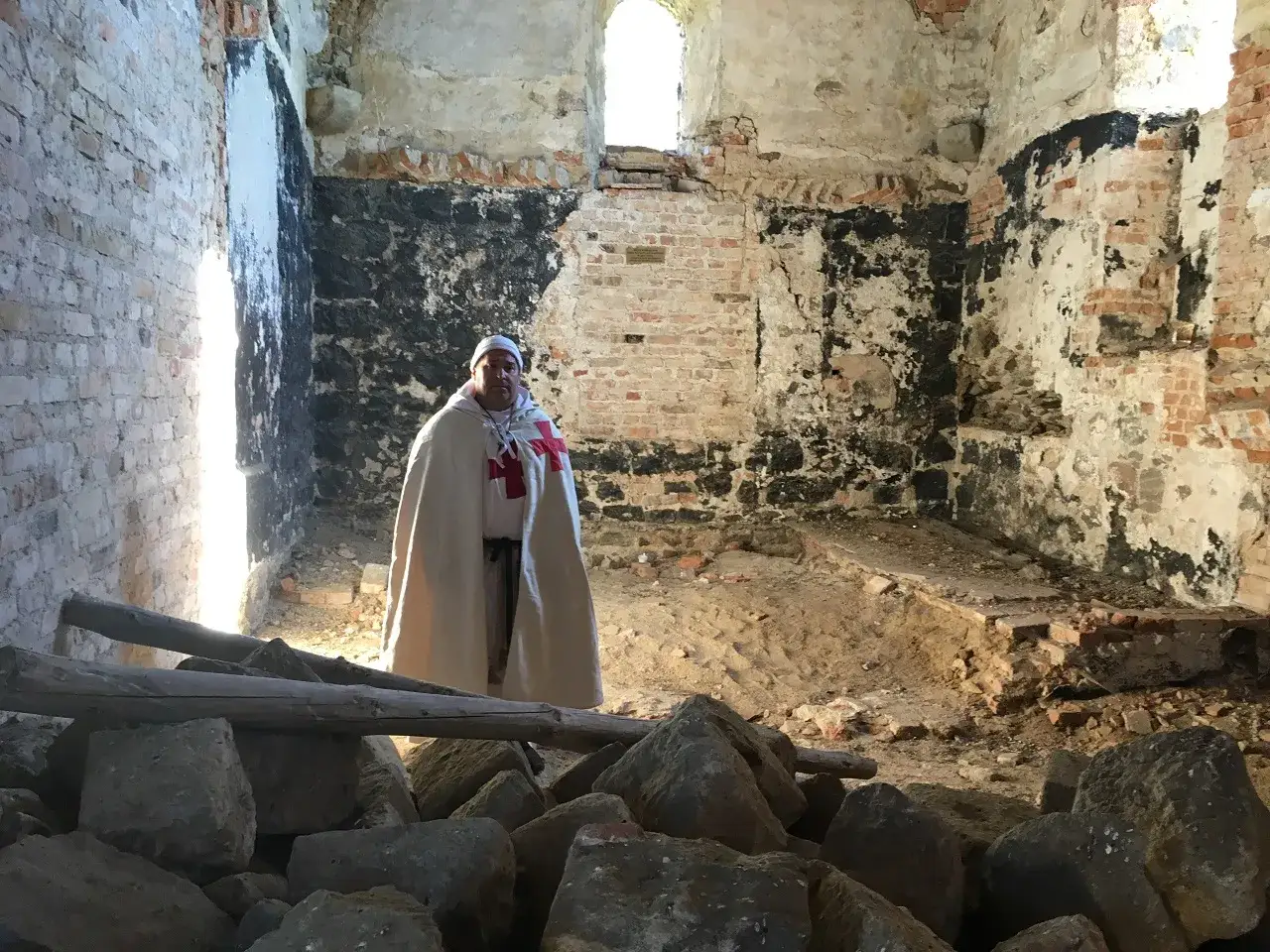 Mężczyzna w stroju templariusza stoi w ruinach zamku.