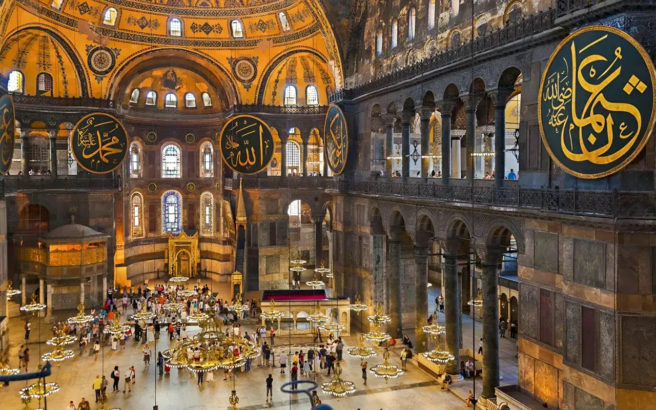 Wnętrze Hagia Sophia, z ogromnymi złotymi kaligrafiami na ciemnych tarczach, przyciąga tłumy turystów.