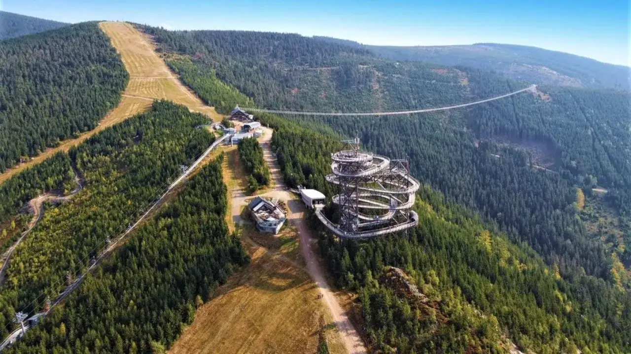Widok na Sky Walk i najdłuższy most w Czechach, zawieszony nad lasem. W oddali widać górskie zbocza.