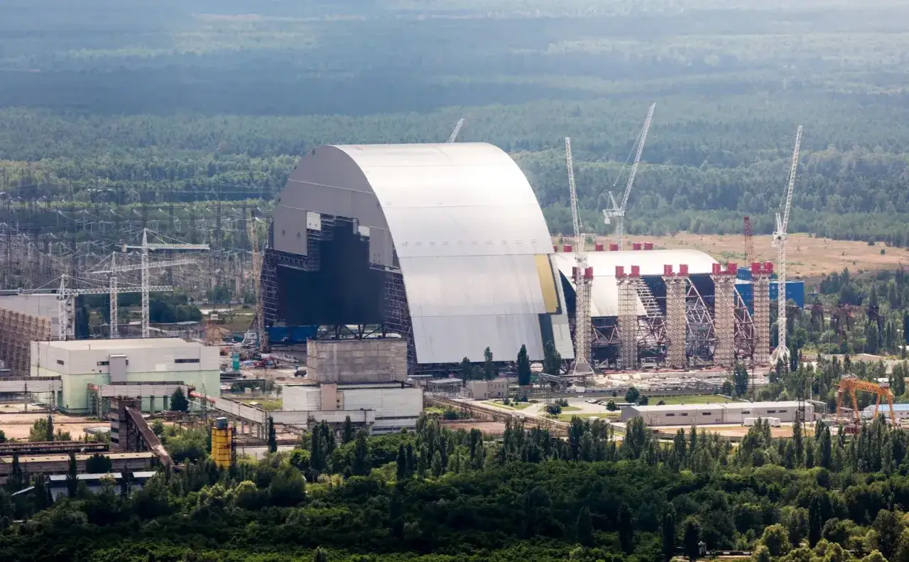 Nowy sarkofag nad reaktorem elektrowni czarnobylskiej, otoczony lasem i dźwigami budowlanymi.