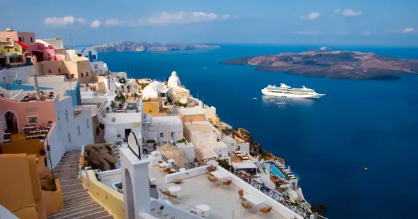 Santorini, Grecja. Białe domy na klifie, błękitne morze i statek wycieczkowy. Planujesz podróż? Pamiętaj o podatku turystycznym Grecja.