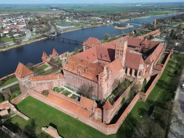 Malbork, największy zamek na świecie, rozciąga się wzdłuż rzeki Nogat. Potężne ceglane mury i wieże świadczą o jego historycznym znaczeniu.
