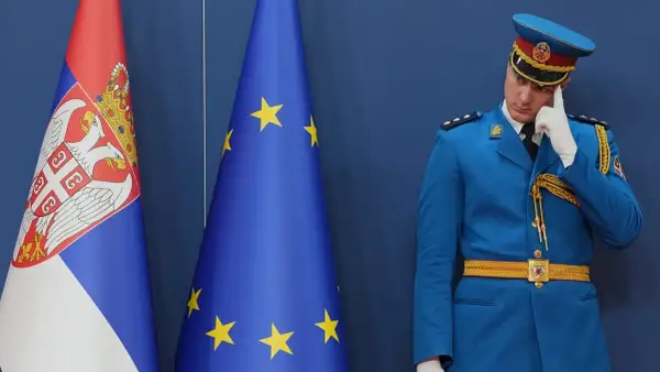 Strażnik w niebieskim mundurze zastanawia się, czy Serbia jest w Unii, stojąc obok flag Serbii i UE.